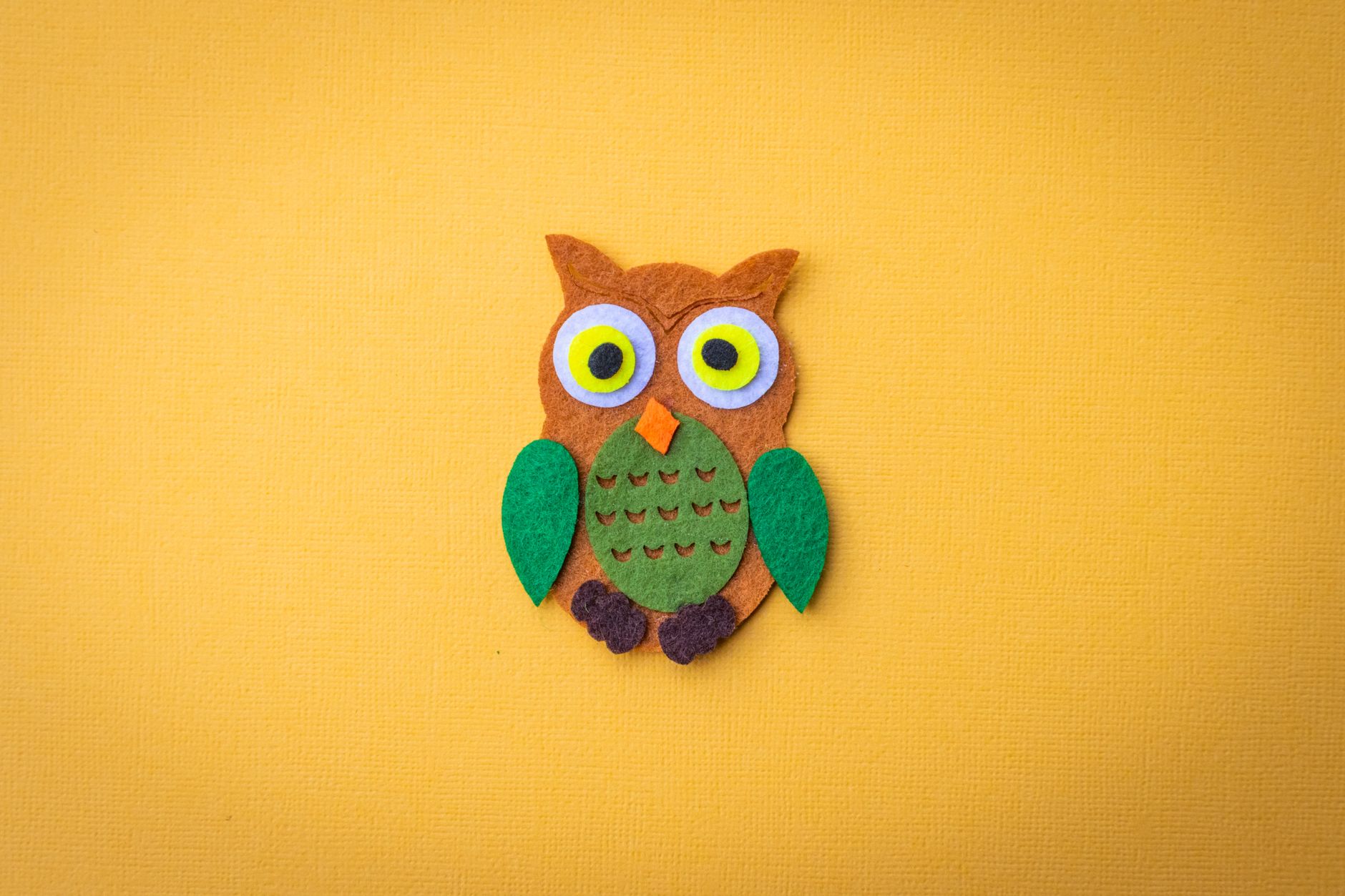 Bright felt owl craft on a vivid yellow backdrop, ideal for design projects.