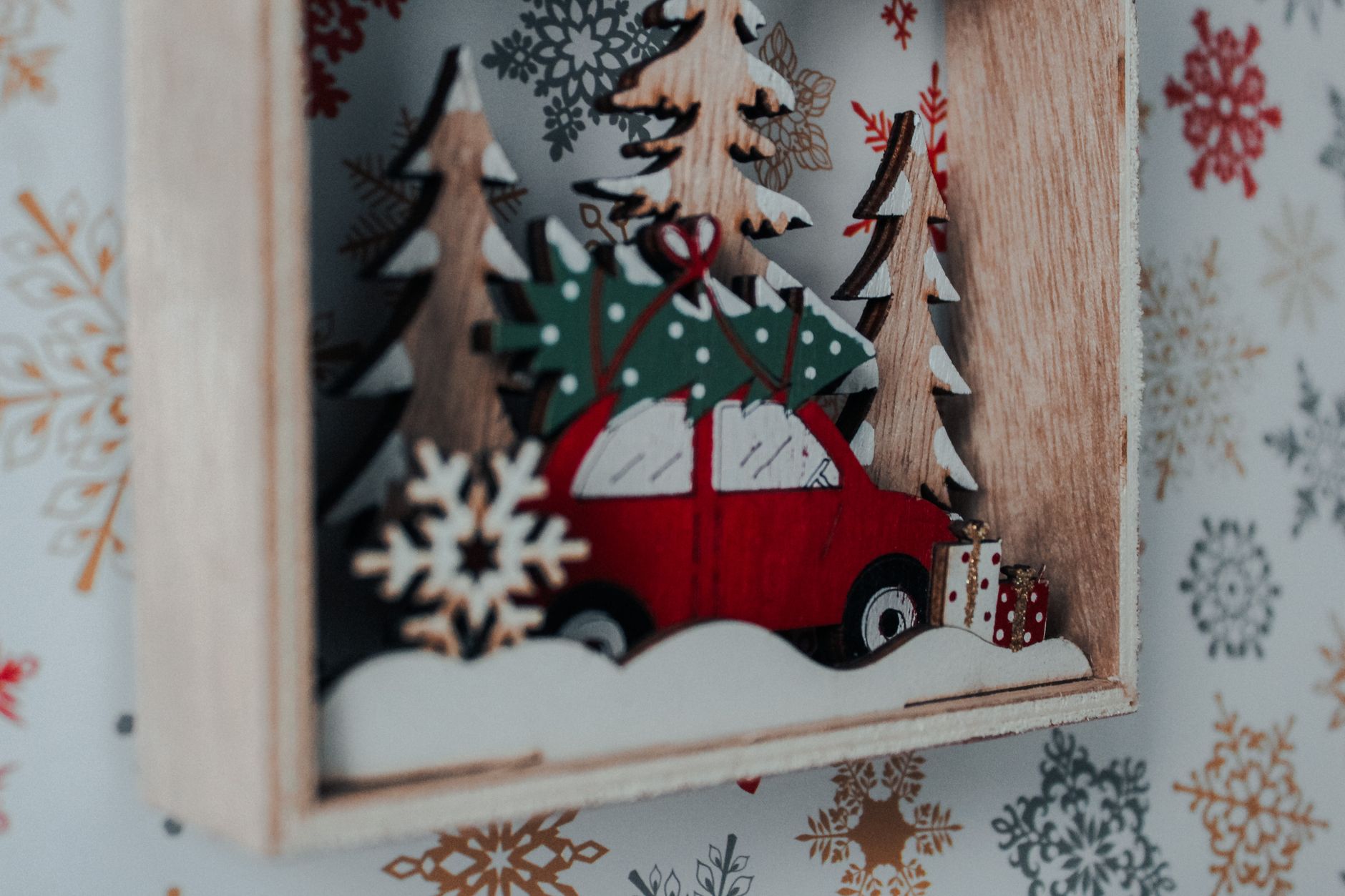 A close-up of a wooden Christmas ornament featuring a car and gift boxes, set against a festive background.