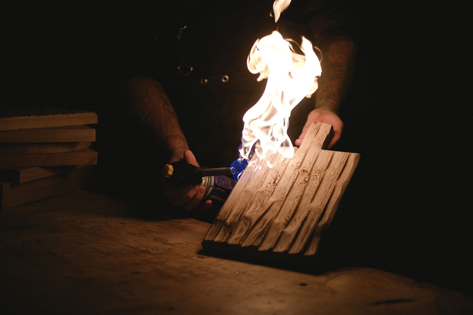Unrecognizable male carpenter burning wooden detail with patterns using gas burner while working in dark professional joinery with special equipment
