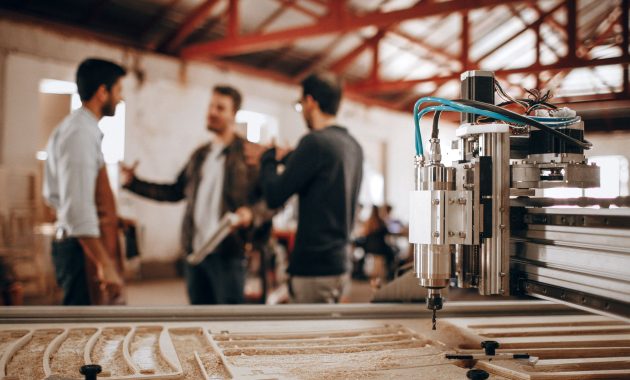 aap-frequently-asked-questions-about-cnc-router-gift-projects-1793155396 Three men discussing work in a woodworking shop with CNC machinery in focus.
