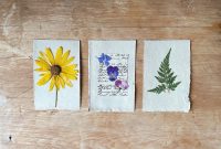 aap-how-to-make-pressed-flower-bookmarks-1791468018 Overhead view of three artistic botanical prints with pressed flowers and leaves on rustic paper.
