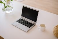aap-how-to-start-a-craft-blog-and-make-money-1791083436 A minimalist workspace with an open laptop, coffee mug, and vase on a bright indoor table.