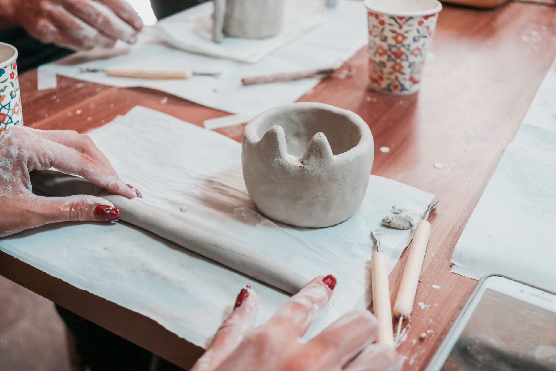 Close-up of hands sculpting pottery with tools in an indoor workshop setting.