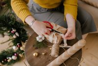 aap-personalized-gift-ideas-using-a-cricut-maker-1790881255 An adult wrapping a Christmas gift with ribbons and decorations at home.