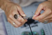 Detailed view of hands crafting handmade jewelry with beads and tools.