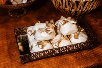 aap-unique-handmade-wedding-favors-guests-will-keep-1791122383 A collection of meticulously wrapped gifts with gold ribbons displayed on a decorative metallic tray.