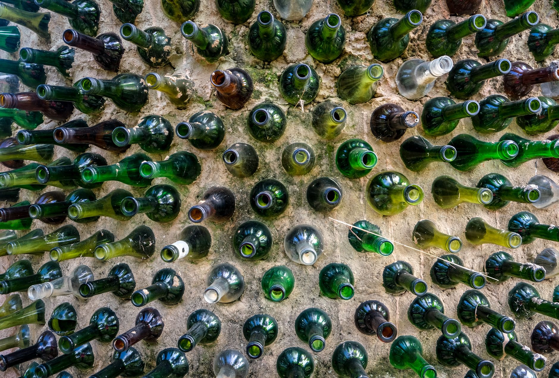 Creative display of empty glass bottles embedded in a wall, forming a colorful pattern.